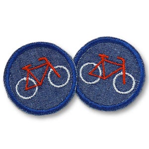 May include: Two round denim patches with a red bicycle design and white wheels. The patches have a blue border and are set against a white background. These patches are ideal for adding to clothing or accessories.