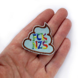 May include: A blue embroidered patch shaped like a pile of poo with the word "FCK NZS" in rainbow colours.