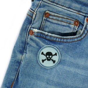 May include: A pair of blue denim jeans with a light blue skull and crossbones patch on the front pocket.