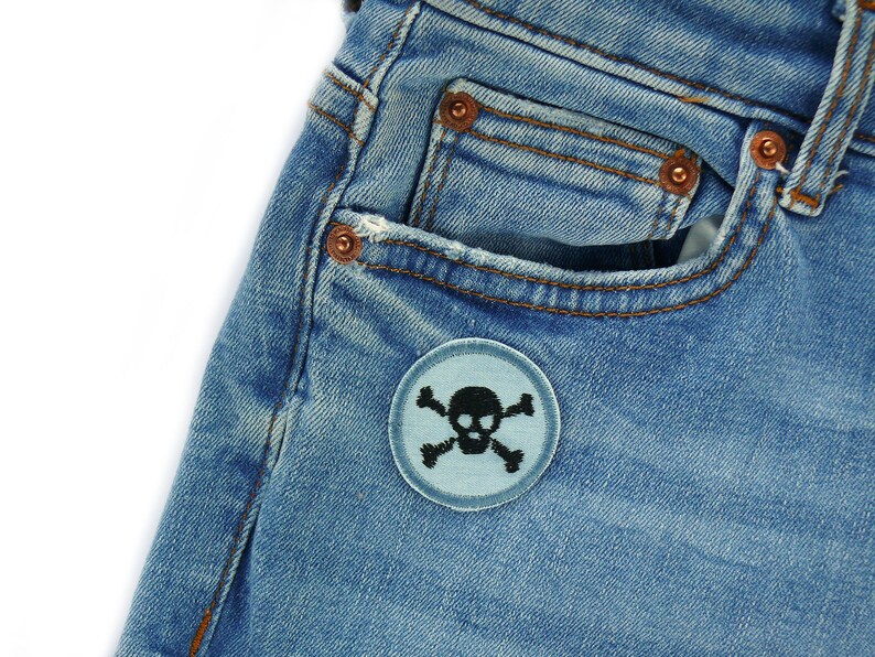 May include: A pair of blue denim jeans with a light blue skull and crossbones patch on the front pocket.