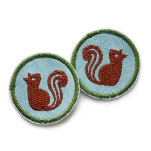 Op de afbeelding: Twee ronde, blauwe en groene geborduurde patches met een bruin eekhoornontwerp.
