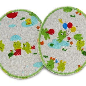 May include: Two round, green-trimmed, beige fabric pads with a frog theme. One pad features frogs with umbrellas and boots, while the other shows frogs with balloons.