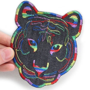 Könnte beinhalten: Ein schwarzer Jeans-Patch mit einem regenbogenfarbenen gestickten Tigergesicht.