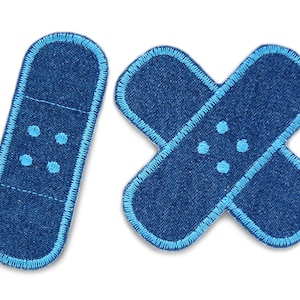 Könnte beinhalten: Zwei blaue Bandagen aus Jeansstoff mit hellblauen Nähten und weißen Punkten. Die Bandagen sind kreuzförmig.
