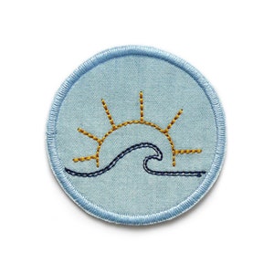 May include: A blue circular patch with a yellow sun and a blue wave embroidered on it.