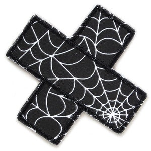 Op de afbeelding: Zwarte stoffen patch in de vorm van een kruis met een wit spinnenwebontwerp.