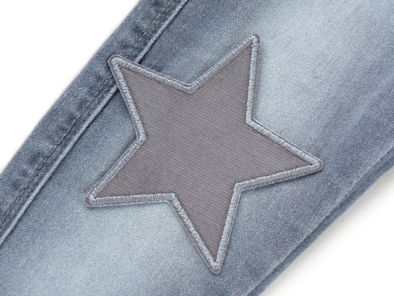Puede incluir: Un par de pantalones vaqueros azules con un parche en forma de estrella gris cosido en la parte delantera.
