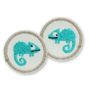 May include: Two circular embroidered patches featuring a bright turquoise chameleon design on a white background. Each patch has a stitched beige border. The chameleon is depicted in profile with a curled tail and a single visible eye in black.