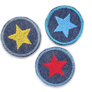 Op de afbeelding: Drie geborduurde patches met sterontwerpen. Elke patch is cirkelvormig met een donkerblauwe denim achtergrond en een lichtblauwe gestikte rand. Eén patch heeft een gele ster, een andere een lichtblauwe ster en de derde een rode ster.