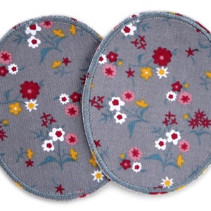 Könnte beinhalten: Zwei graue ovale Stoffpatches mit einem Blumenmuster. Das Muster zeigt kleine weiße, rosa und rote Blumen mit gelben und türkisfarbenen Akzenten auf grauem Hintergrund.