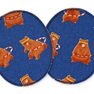 Op de afbeelding: Twee blauwe stoffen cirkels met een witte rand. Elke cirkel heeft een herhalend patroon van bruine beren die rode en witte hoepels dragen.