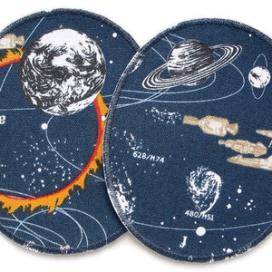 May include: Two round, blue fabric patches with a space theme. One patch features a planet with a red and yellow ring around it. The other patch features a planet with rings and a spaceship. Both patches have white stars and white text.