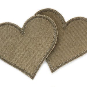 Può includere: Due toppe a forma di cuore in feltro marrone con un bordo cucito.