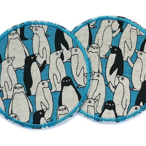 May include: Two round blue and white fabric coasters with a pattern of black and white penguins. The coasters have a turquoise blue border.