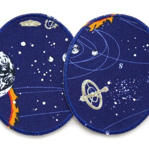 May include: Two round blue fabric patches with white stars and a space-themed design. One patch features a planet with a fiery tail and the other features a stylised solar system with a compass.
