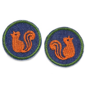 May include: Two round embroidered iron-on patches with a green outer border and a blue denim centre. Each patch features a stylised orange squirrel.