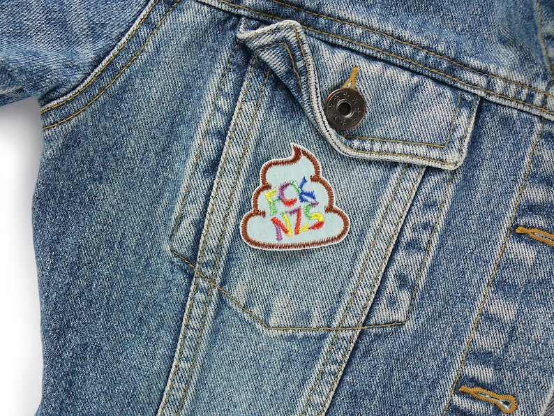May include: A blue denim jacket with a colorful embroidered patch of a pile of poop with the word "FCK NZS" on it.