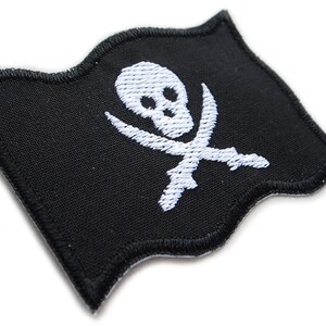 Peut inclure: Un patch de drapeau de pirate en tissu noir avec un motif de cr&acirc;ne et d'os crois&eacute;s blancs. Le drapeau est brod&eacute; et a un bord ondul&eacute;.