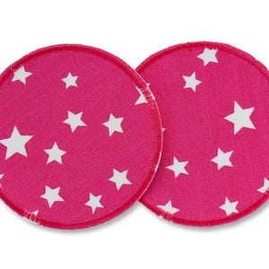 May include: Two pink fabric nursing pads with white stars printed on them. The pads are round and have a white stitched edge.