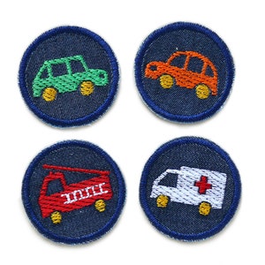 May include: Four embroidered patches featuring vehicle designs. Each patch is a dark blue circle with a light blue border. The vehicles include a green car, an orange car, a red fire engine, and a white ambulance with a red cross.