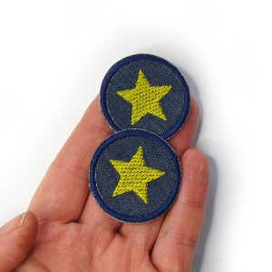 Peut inclure: Deux patchs en denim bleu avec des étoiles brodées jaunes. Les patchs sont ronds et ont une bordure bleu foncé.
