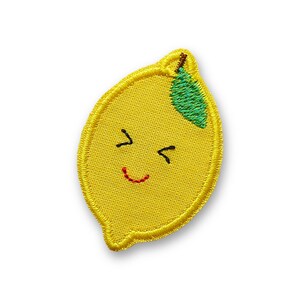 Peut inclure: Un écusson brodé en forme de citron jaune avec une feuille verte cousue sur le dessus. Le citron présente un visage brodé simple composé de deux lignes noires pour les yeux fermés et d'une petite ligne rouge incurvée pour la bouche.