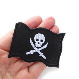 Peut inclure: Un drapeau de pirate en tissu noir avec un motif de cr&acirc;ne et d'os crois&eacute;s brod&eacute;s en blanc.