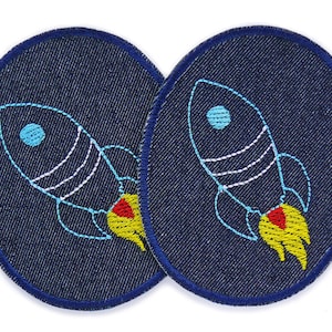 Könnte beinhalten: Zwei blaue Jeans-Patches mit weißen und gelben gestickten Raketen. Jede Rakete hat einen blauen Kreis in der Mitte und eine rote und gelbe Flamme.