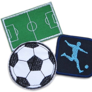 Op de afbeelding: Drie geborduurde patches met een voetbal, een voetballer en een groen voetbalveld. De patches zijn allemaal wit met zwarte stiksels.