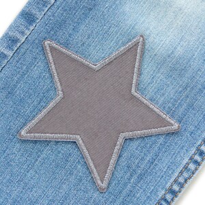 Puede incluir: Primer plano de un par de pantalones vaqueros azules con un parche en forma de estrella gris cosido en la parte delantera.