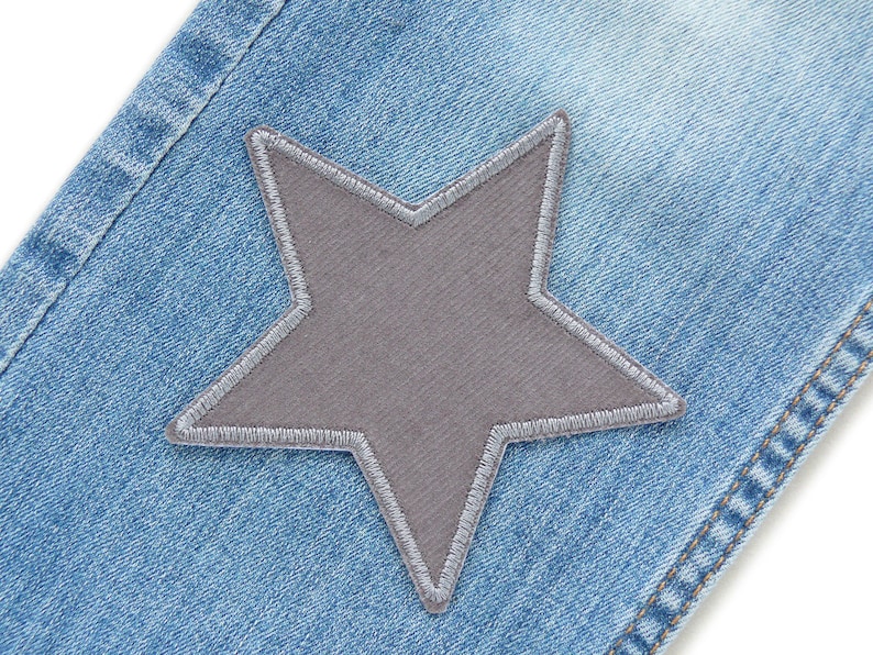 Puede incluir: Primer plano de un par de pantalones vaqueros azules con un parche en forma de estrella gris cosido en la parte delantera.