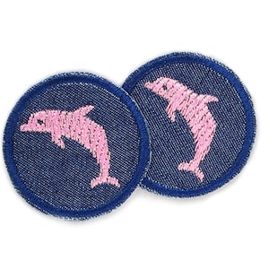May include: Two round blue denim patches with pink embroidered dolphin silhouettes.