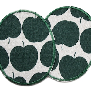 Op de afbeelding: Twee ronde stoffen onderzetters met een groen appelmotief op een witte achtergrond en groene stiksels rond de randen.