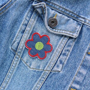 May include: A blue denim jacket with a red and blue flower patch on the pocket. The flower has a yellow center.