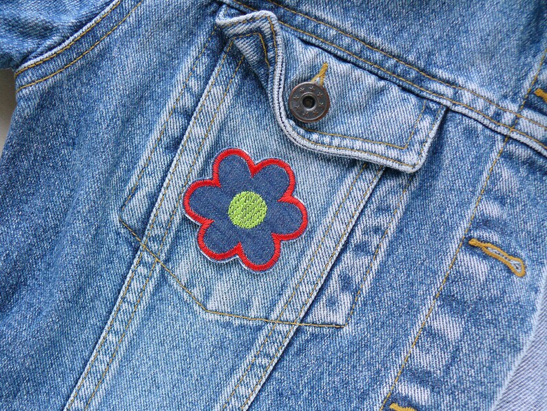 May include: A blue denim jacket with a red and blue flower patch on the pocket. The flower has a yellow center.