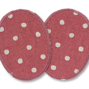 May include: Two pink fabric elbow pads with white polka dots. The pads are oval shaped and have a stitched edge.
