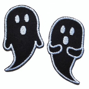 Op de afbeelding: Twee zwarte vilt-geestpatches met witte geborduurde ogen en monden. De geesten zijn omrand met wit garen.