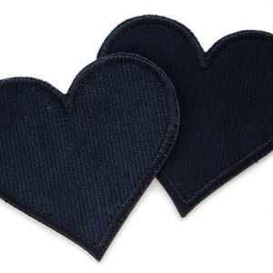 Könnte beinhalten: Zwei schwarze Filz-Herz-Patches mit einem genähten Rand.