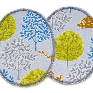 Könnte beinhalten: Zwei runde Stoffpatches mit grauem Hintergrund und einem sich wiederholenden Muster aus gelben, blauen und grauen Bäumen. Ein Patch hat einen kleinen orangefarbenen Igel in der oberen rechten Ecke.
