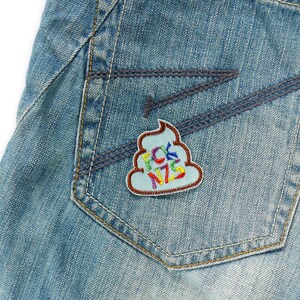 May include: A blue denim jean pocket with a colorful embroidered patch shaped like a pile of poop with the text "FCK NZS" on it.