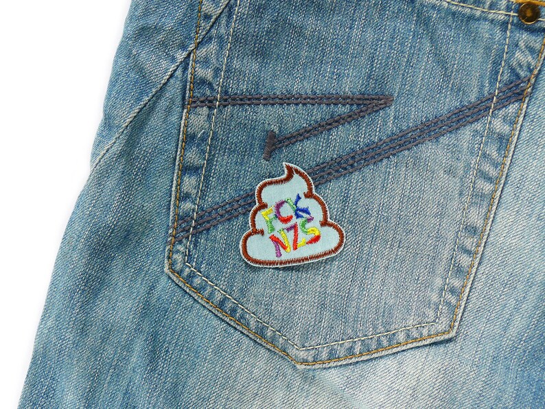 May include: A blue denim jean pocket with a colorful embroidered patch shaped like a pile of poop with the text "FCK NZS" on it.