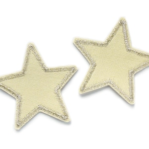 Può includere: Due stelle in tessuto beige con bordo glitterato argento.