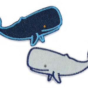 May include: Two embroidered whale patches. The top whale is dark navy blue with a bright blue border and a small orange eye. The bottom whale is light grey with a dark navy blue border and a small grey eye. Both feature detailed stitching.