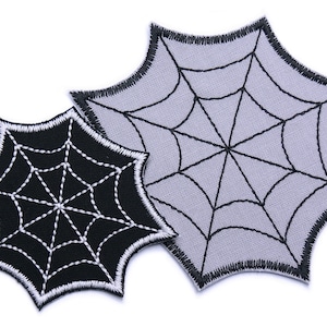 Könnte beinhalten: Zwei gestickte Spinnennetz-Patches, einer schwarz mit weißen Nähten und einer grau mit schwarzen Nähten.