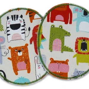 May include: Two circular fabric coasters featuring a cream background and a pattern of cartoon animals, such as a zebra, bear, and lion. Each coaster has a green stitched border. The animals are in vibrant colours.