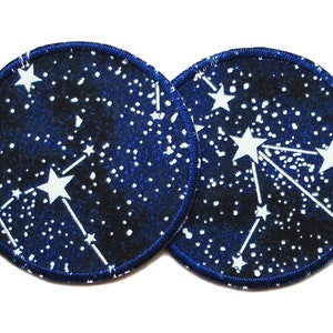 May include: Two round blue fabric patches with white stars and a constellation design. The patches have a dark blue border.