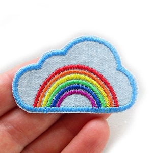 Può includere: Una toppa di feltro blu con un arcobaleno ricamato su di essa. L'arcobaleno è fatto di filo rosso, arancione, giallo, verde, blu, indaco e viola. La toppa ha la forma di una nuvola.