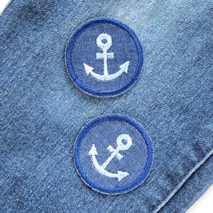 May include: Two blue denim patches with white embroidered anchors. The patches are sewn onto a blue denim fabric.