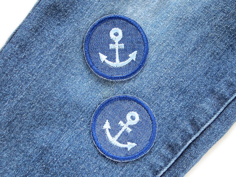May include: Two blue denim patches with white embroidered anchors. The patches are sewn onto a blue denim fabric.