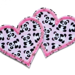 May include: Two pink fabric hearts with a white background and a black and white panda bear pattern. The hearts have a pink stitched border.